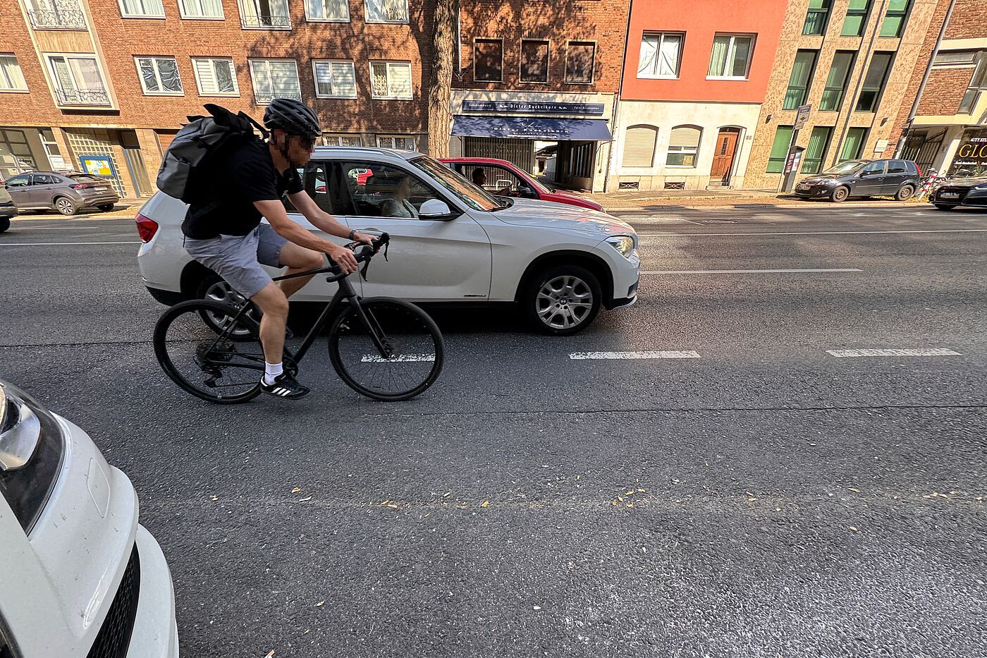 Ein Radfahrer fährt auf der rechten Fahrspur der Wilhelmstraße neben einem weißen Auto. Die Straße ist mehrspurig, es gibt keinen baulich geschützten Radweg.