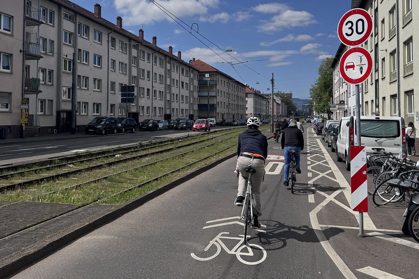 Radfahrende fahren auf einer Fahrbahn mit Fahrradpiktogrammen. Ein Verkehrszeichen weist auf Tempo 30 und ein Überholverbot gegenüber einspurigen Fahrzeugen hin.