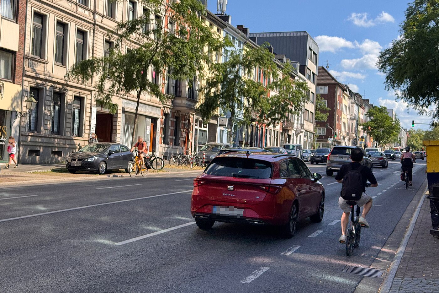 Zwei Radfahrende fahren auf der Wilhelmstraße neben Autos und einem Lieferfahrzeug. Die Radverkehrsführung ist schmal markiert und liegt unmittelbar neben dem Kfz-Verkehr.
