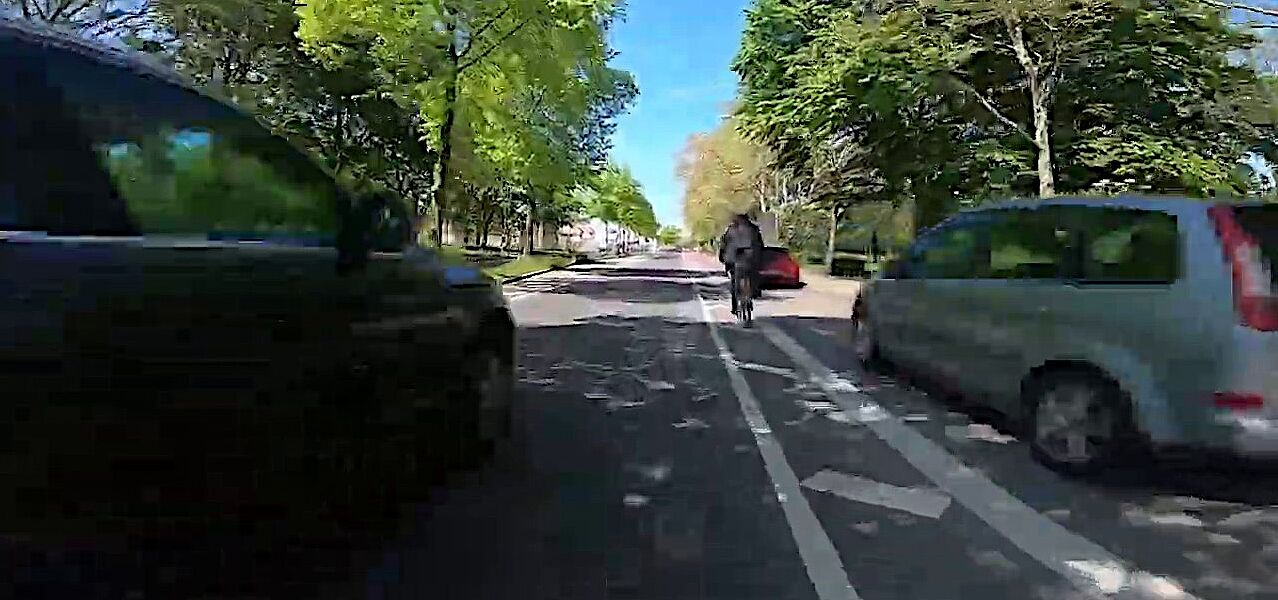 Stellungnahme von ADFC/ProRad Düren zur Veldener Straße Ein Fahrradfahrer fährt neben einem zugeparkten Radstreifen, während sich ein weiteres Kfz von hinten nähert