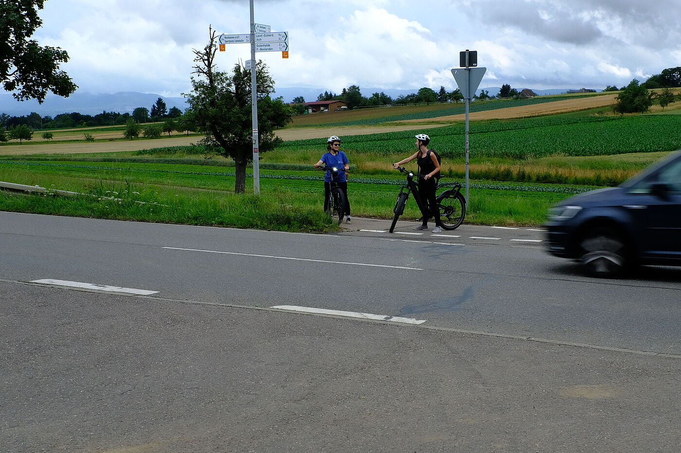Kreuzungsbereich an einer Landstraße und zwei Radfahrende