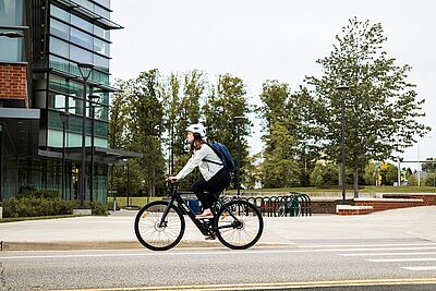 Eine Frau fährt auf einem exakt auf sie eingestellten Fahrrad. Vor ihr ist ein Bürogebäude zu sehen.