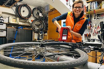 Eine Person codiert ein Fahrrad in einer Werkstatt. Dabei wird mit einem Gerät ein Code gut sichtbar auf den Rahmen des Fahrrads durch Prägung, Gravur oder Klebung aufgebracht. Das soll der Diebstahlprävention dienen.