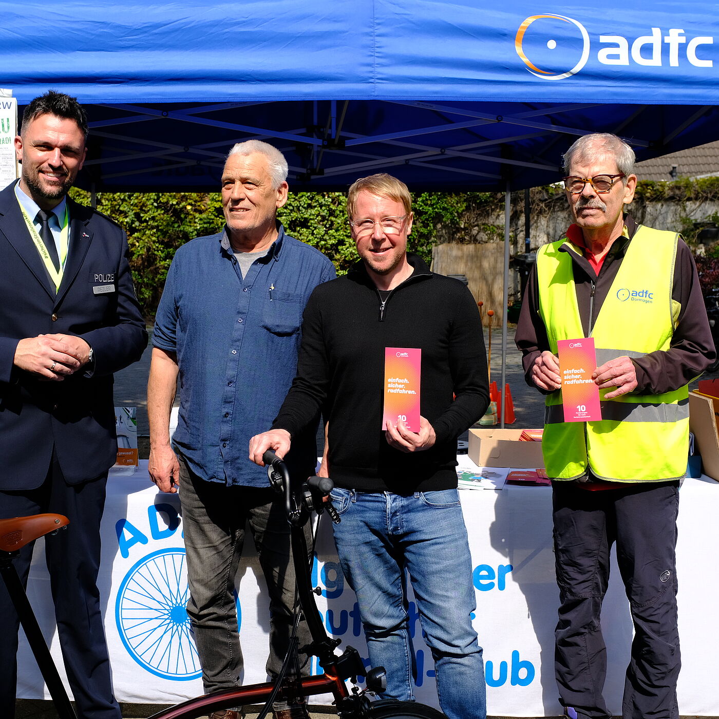 2026-04-17_Dormagen_Verkehrssicherheit__ADFC_NRW Vier Personen /ein Polizist vor einem ADFC Stand.
