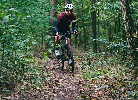Ein Gravelbiker fährt auf einem schmalen Waldpfad.