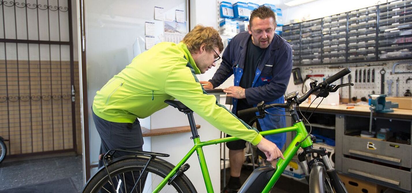 Ein Kunde zeigt dem Mechaniker in einer Werkstatt einen Defekt am Rad. 