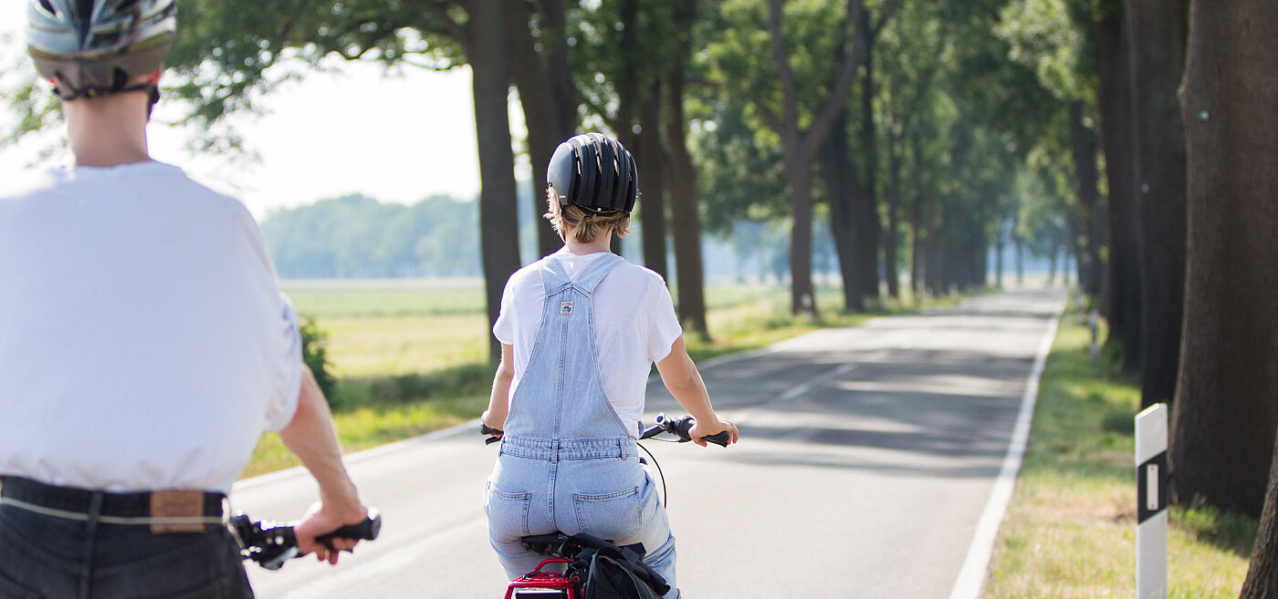 Radfahrende auf einer Landstraße Zwei Personen mit Fahrradhelmen fahren auf einer schmalen Landstraße ohne separaten Radweg.