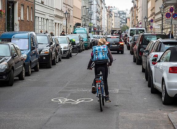 Mädchen auf dem Fahrrad fährt durch eine auf beiden Seiten zugeparkte Straße. 